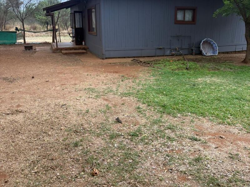 Rear view of a detached house featuring timber cladding, a corrugated metal roof, and a small covered patio area set within a large garden.