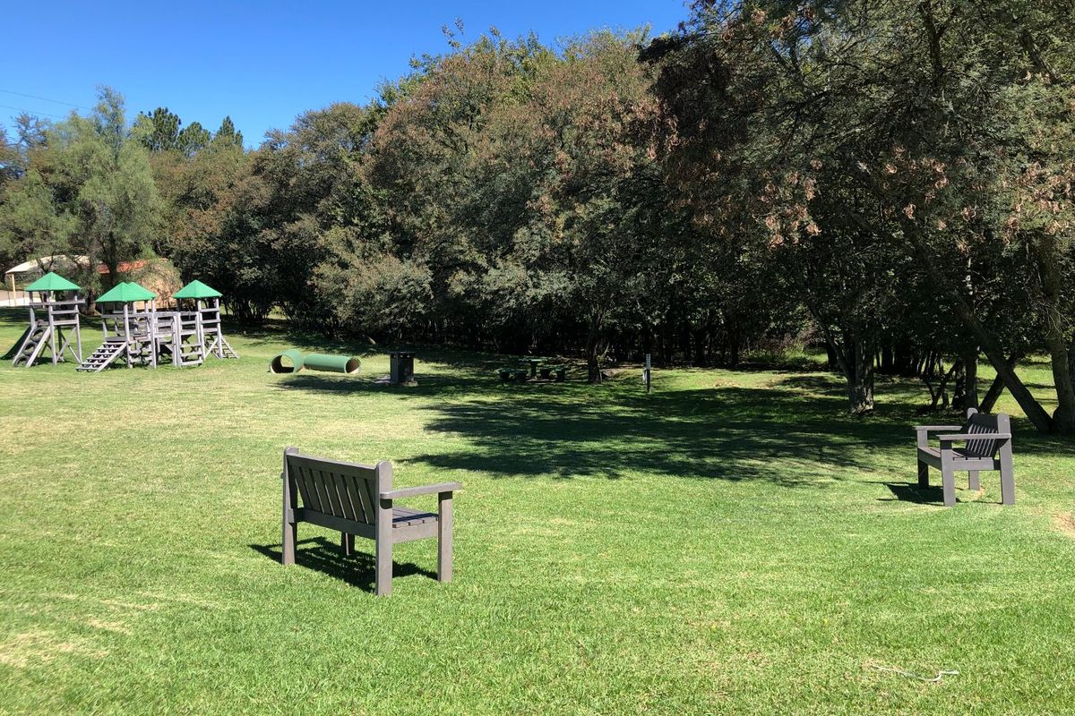 A spacious, well-maintained communal garden area featuring mature trees, a grassy lawn, and playground equipment.