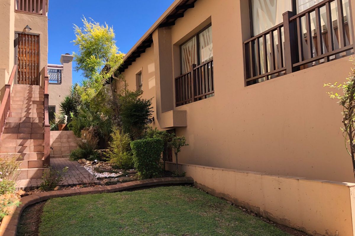 Rear exterior view featuring a paved walkway, landscaped garden, and a tiled staircase with wooden balustrades leading to the upper level.
