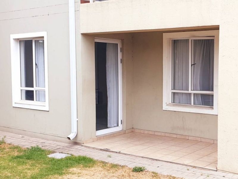 A covered ground-floor patio featuring tiled flooring, direct access to the interior via a sliding door, and adjacent garden space.