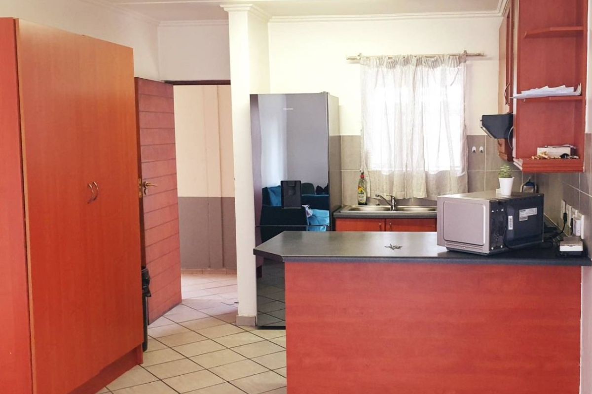 A functional kitchen featuring wood-finish cabinetry, laminate countertops, a breakfast bar, and tiled flooring, providing a practical layout for daily meal preparation.