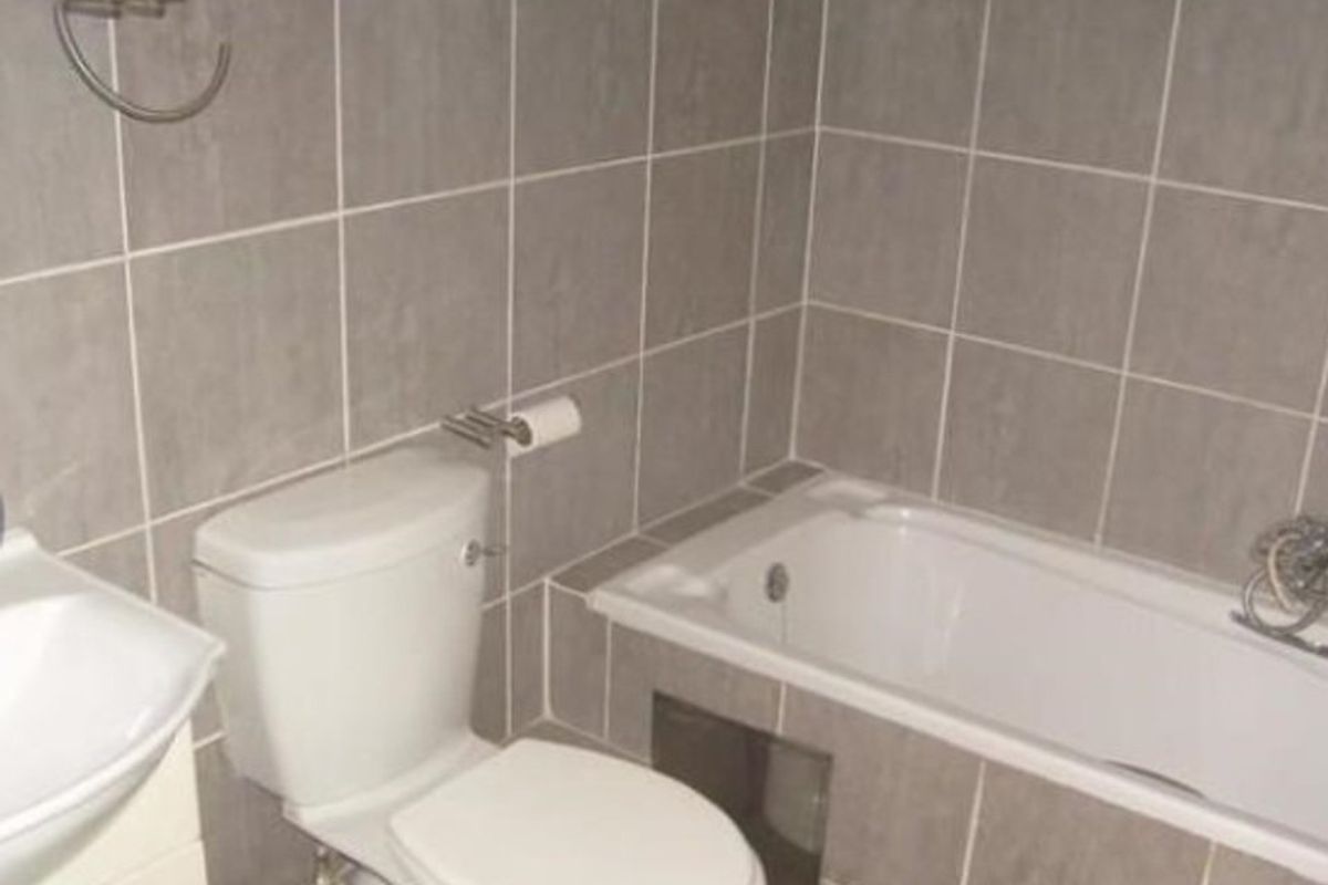 A functional bathroom featuring grey wall tiles, a built-in bathtub, a standard toilet, and a wall-mounted washbasin.
