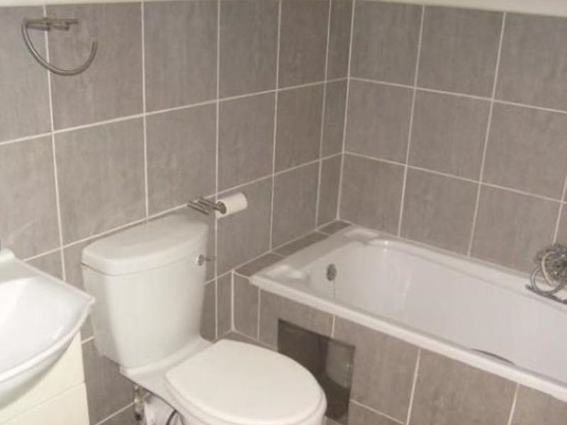A functional bathroom featuring grey wall tiles, a built-in bathtub, a standard toilet, and a wall-mounted washbasin.