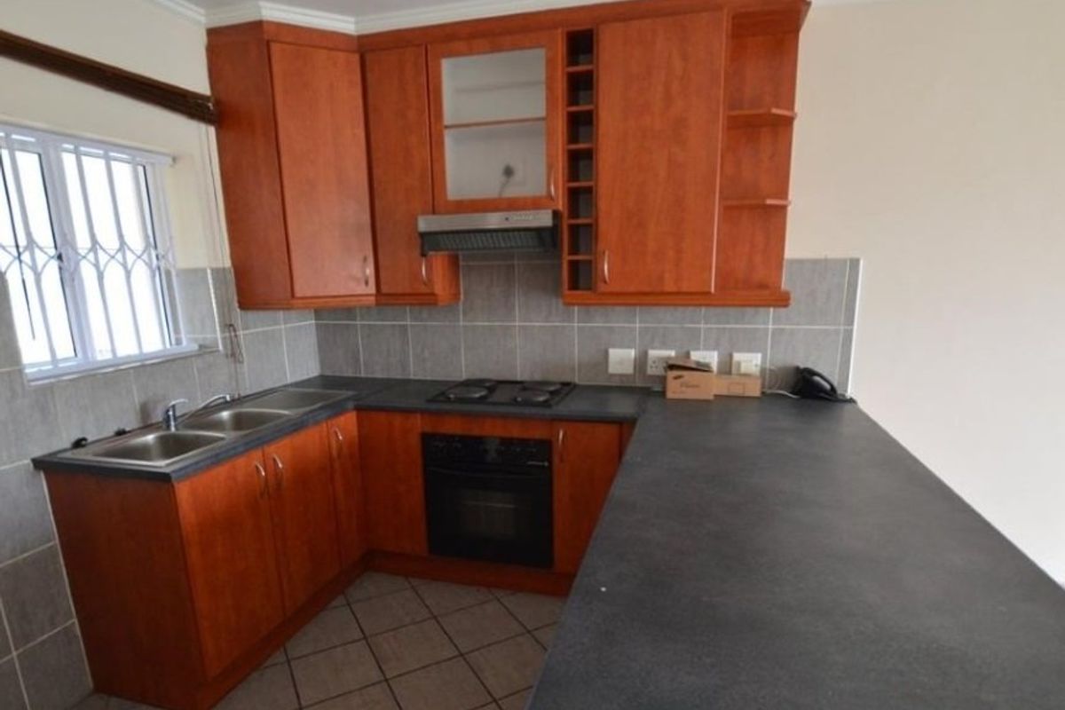 A functional kitchen featuring wood-finish cabinetry, dark laminate countertops, a built-in oven with hob, and a double basin sink with tiled backsplash.