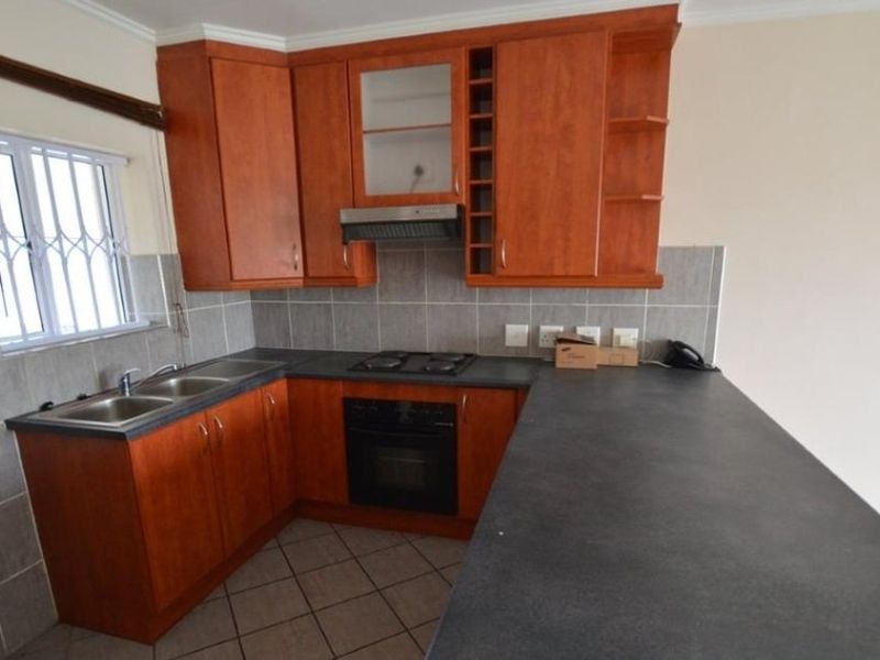 A functional kitchen featuring wood-finish cabinetry, dark laminate countertops, a built-in oven with hob, and a double basin sink with tiled backsplash.