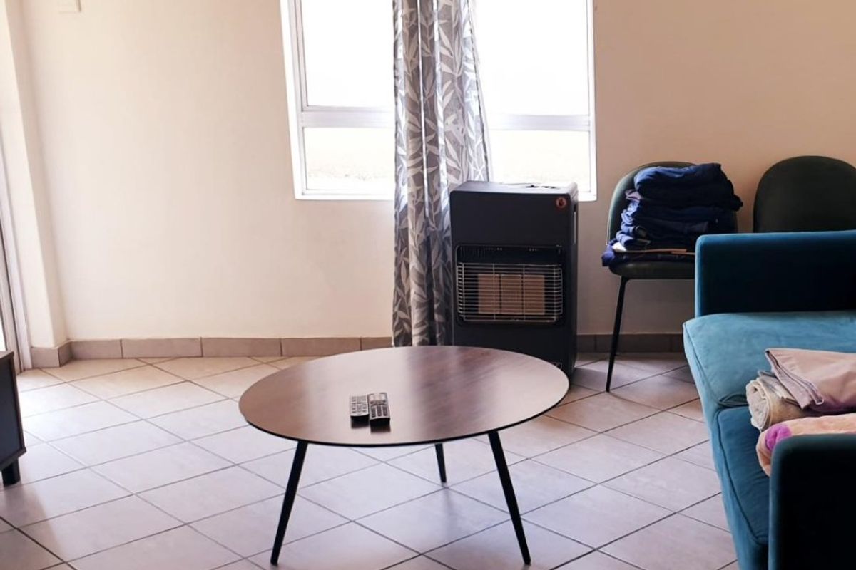 A living room area featuring neutral tiled flooring and a large window, providing a functional and well-lit space.