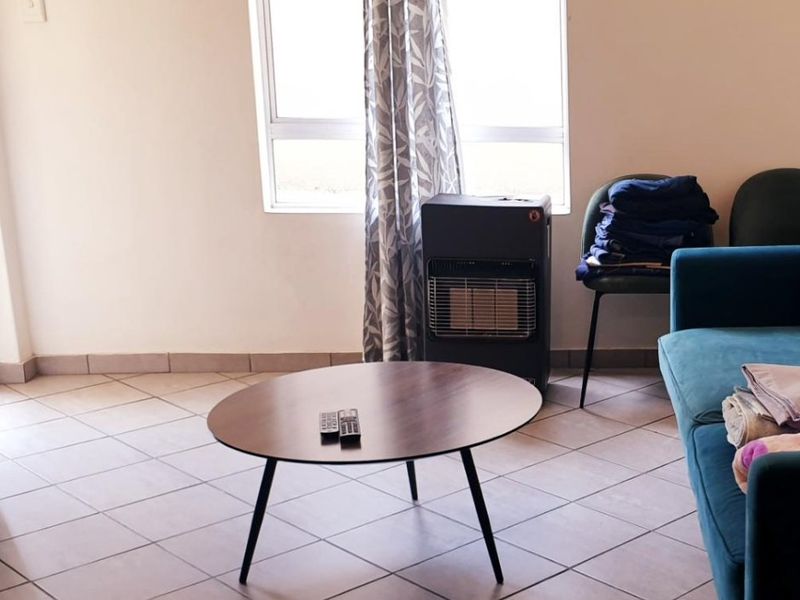 A living room area featuring neutral tiled flooring and a large window, providing a functional and well-lit space.