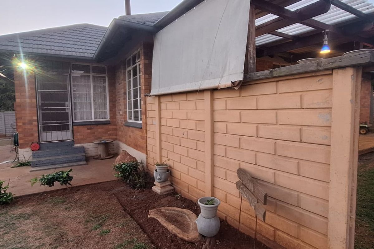 Rear view of the house featuring a brick facade, a covered patio area, and a concrete boundary wall in the garden.