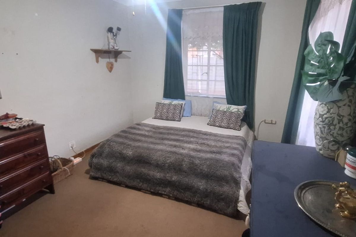 A standard bedroom featuring carpeted flooring and security bars on the windows, providing a functional and private sleeping space.