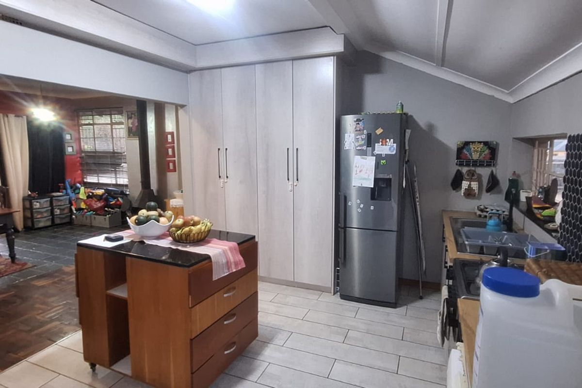 A functional kitchen featuring light-toned built-in cabinetry, a modern hexagonal tile backsplash, and tiled flooring, with an open-plan layout connecting to the adjacent living area.