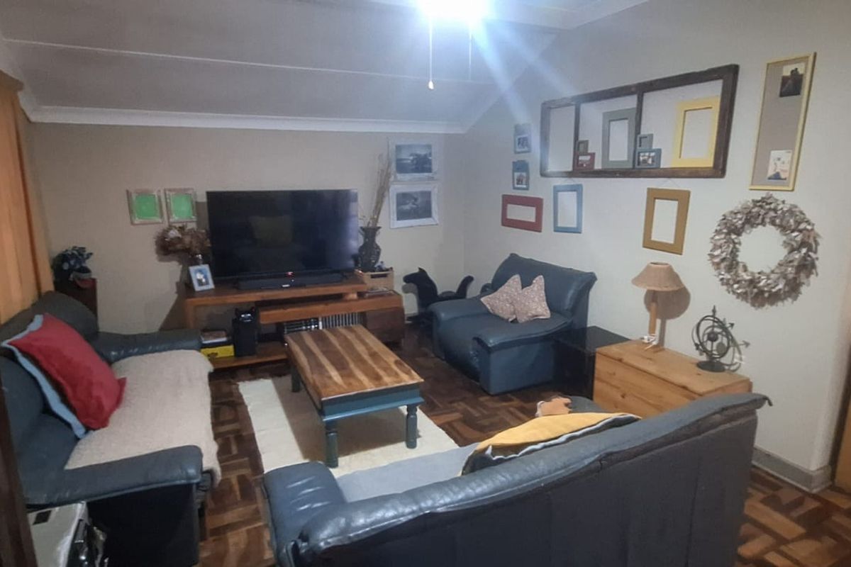 A cozy living room featuring classic parquet flooring, a coved ceiling, and a ceiling fan, with an open transition to the adjacent kitchen area.