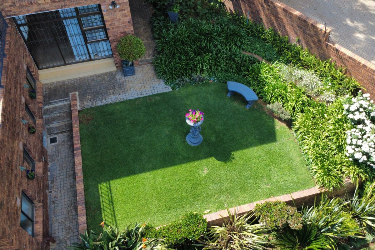 An elevated view of a well-maintained rear garden featuring a manicured lawn, paved pathways, and established perimeter brick walls.