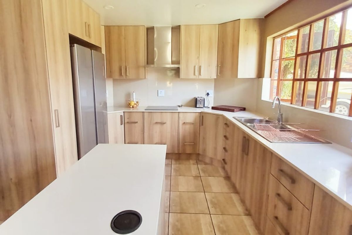 A well-maintained kitchen featuring light wood-look cabinetry, a central island, stainless steel extractor fan, and tiled flooring with ample natural light.