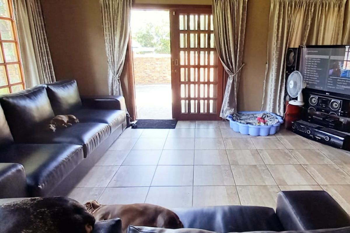 A living room featuring tiled flooring, wooden framed windows, and sliding glass doors providing access to the exterior.