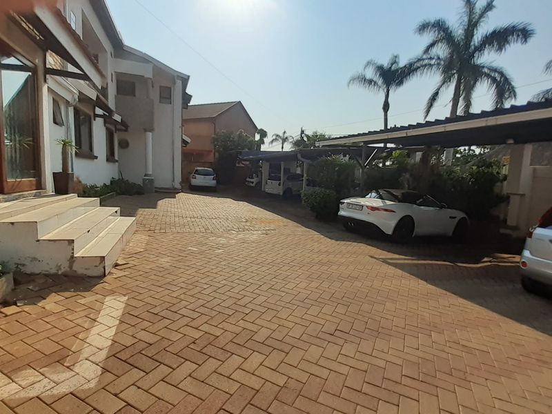 A paved driveway leading to the front entrance of the house, featuring a covered carport area and concrete steps.