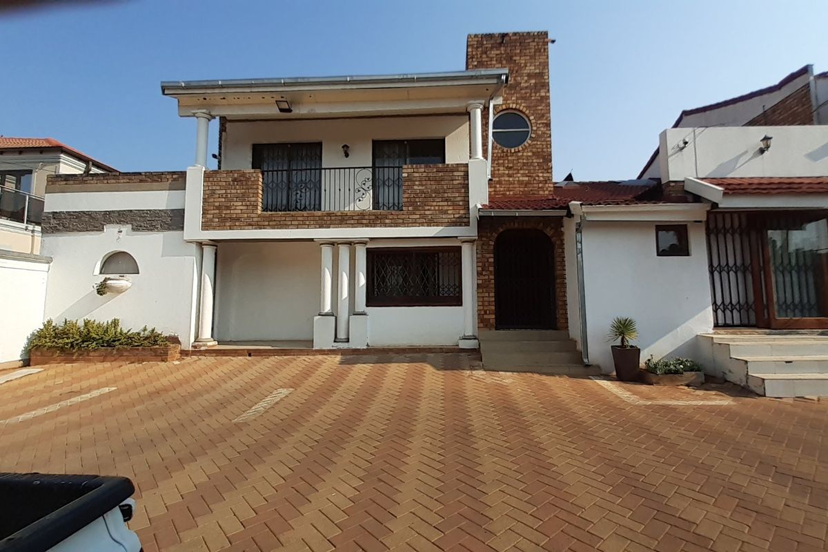 Front elevation of a multi-level house featuring a paved driveway, brick facade, balcony, and secure entrance with decorative columns.