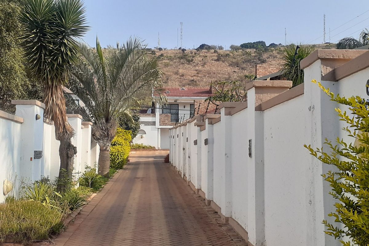A paved driveway leading to the property entrance, flanked by a secure perimeter boundary wall with integrated lighting and electric fencing.