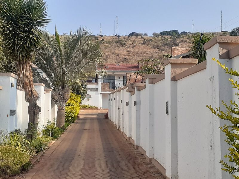 A paved driveway leading to the property entrance, flanked by a secure perimeter boundary wall with integrated lighting and electric fencing.