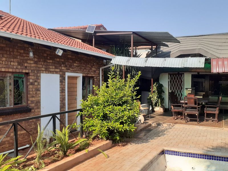 Rear exterior view featuring a brick house, paved patio area, swimming pool, and a covered outdoor entertainment space with metal roofing.