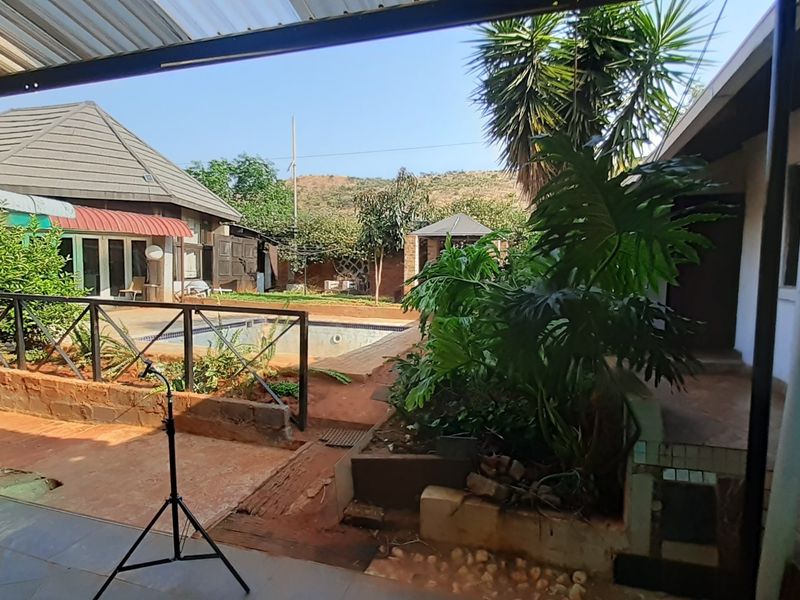 Covered patio area overlooking a swimming pool and rear garden, featuring tiled flooring and metal structural elements.