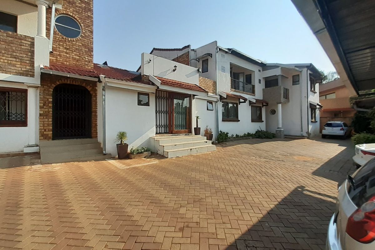 Front exterior view of a multi-level residential property featuring a brick-paved driveway, security gates, and a covered carport area.