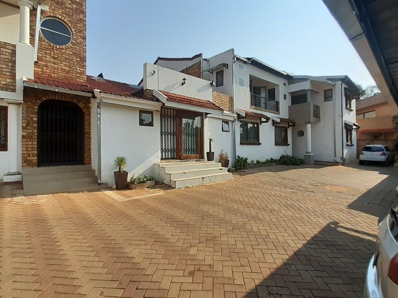 Front exterior view of a multi-level residential property featuring a brick-paved driveway, security gates, and a covered carport area.