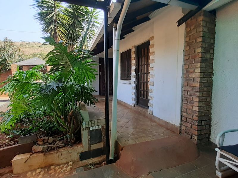 A covered outdoor patio area featuring tiled flooring and brick accents, providing direct access to the garden and pool area.