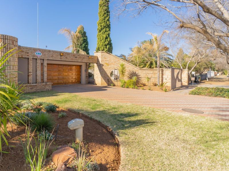 A well-maintained front exterior featuring a brick facade, paved driveway, and a secure garage entrance with established garden landscaping.
