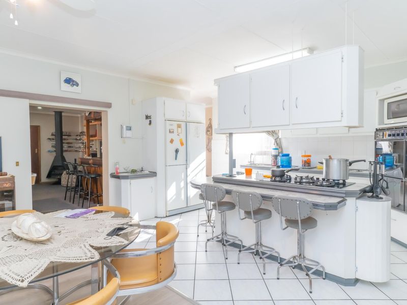 Open-plan kitchen and dining area featuring white cabinetry, a breakfast bar, gas hob, and built-in oven, with tiled flooring throughout.