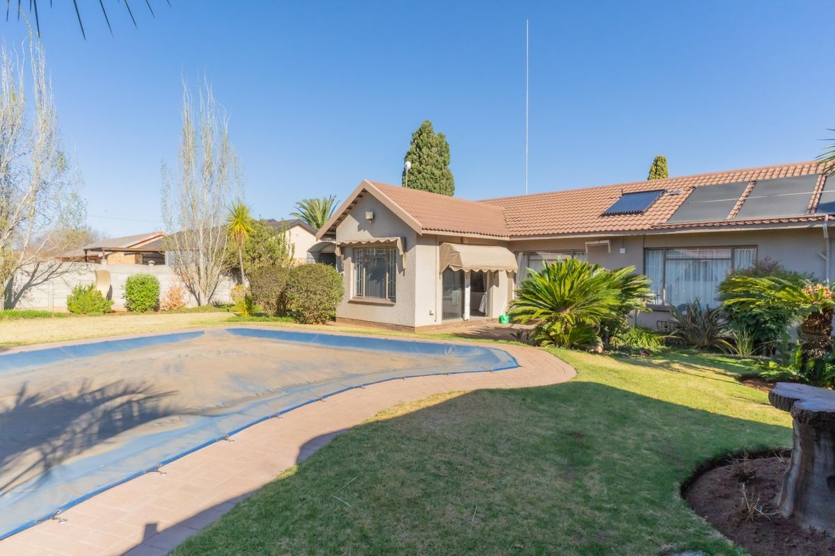 Rear view of the property featuring a swimming pool with a cover, landscaped garden, and solar water heating panels installed on the tiled roof.