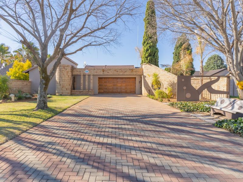 Front view of the property featuring a paved brick driveway, double garage, and well-maintained face brick facade with established landscaping.