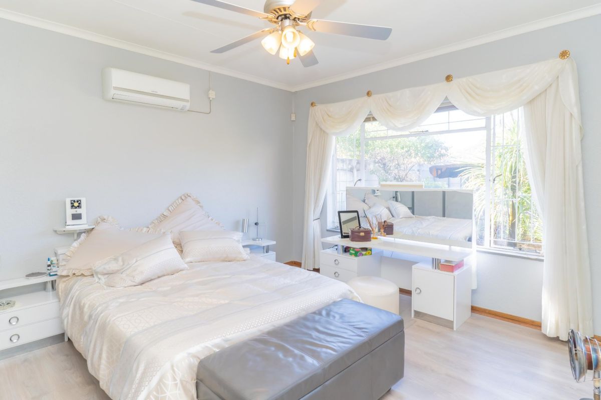 A well-maintained bedroom featuring light laminate flooring, a ceiling fan, and a wall-mounted air conditioning unit.