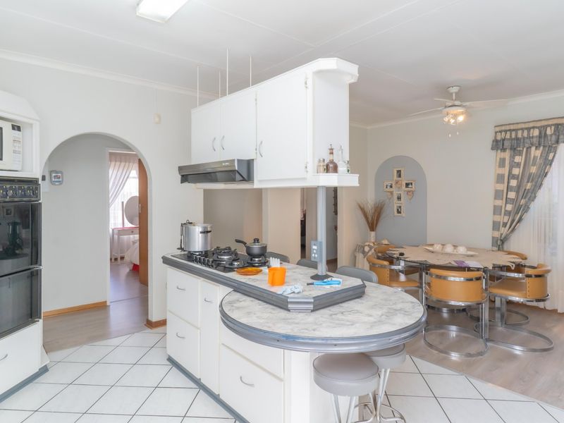 Open-plan kitchen and dining area featuring a central island with gas cooktop, built-in double oven, and classic archway architectural details.