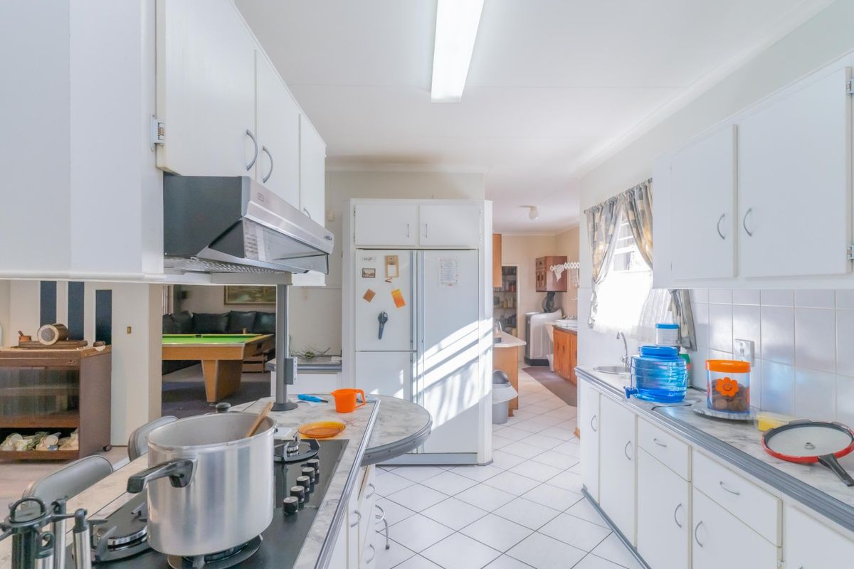 A functional kitchen featuring white cabinetry, laminate countertops, a gas cooktop with extractor fan, and tiled flooring, with an open layout leading to living areas.