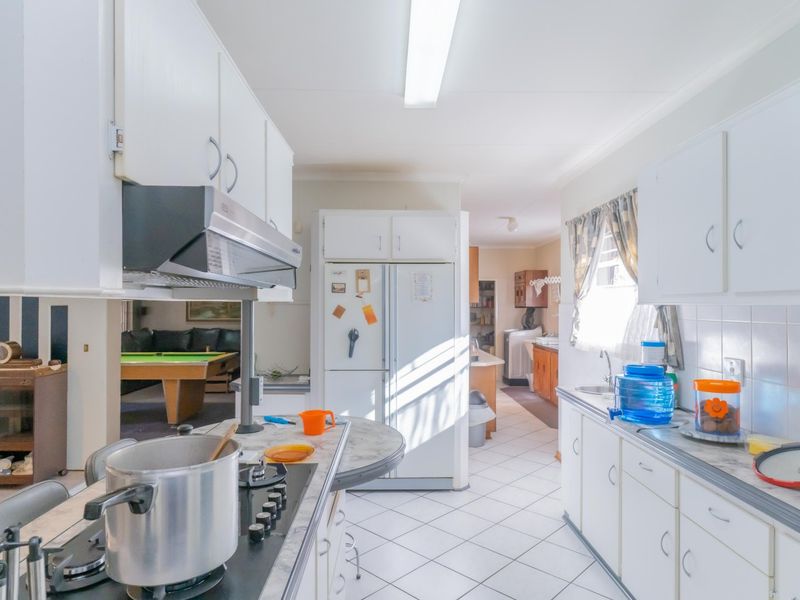 A functional kitchen featuring white cabinetry, laminate countertops, a gas cooktop with extractor fan, and tiled flooring, with an open layout leading to living areas.