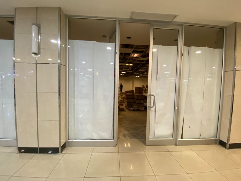Commercial entrance featuring tiled flooring and glass sliding doors, leading into an open-plan space with visible ceiling infrastructure.