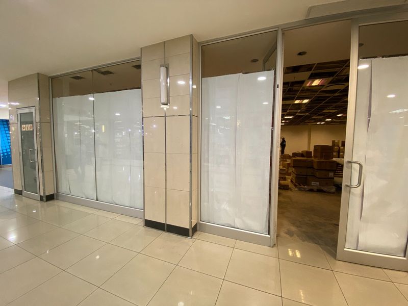 Commercial storefront entrance with tiled flooring and glass doors, showing an unfinished interior space with exposed ceiling grid and missing tiles.