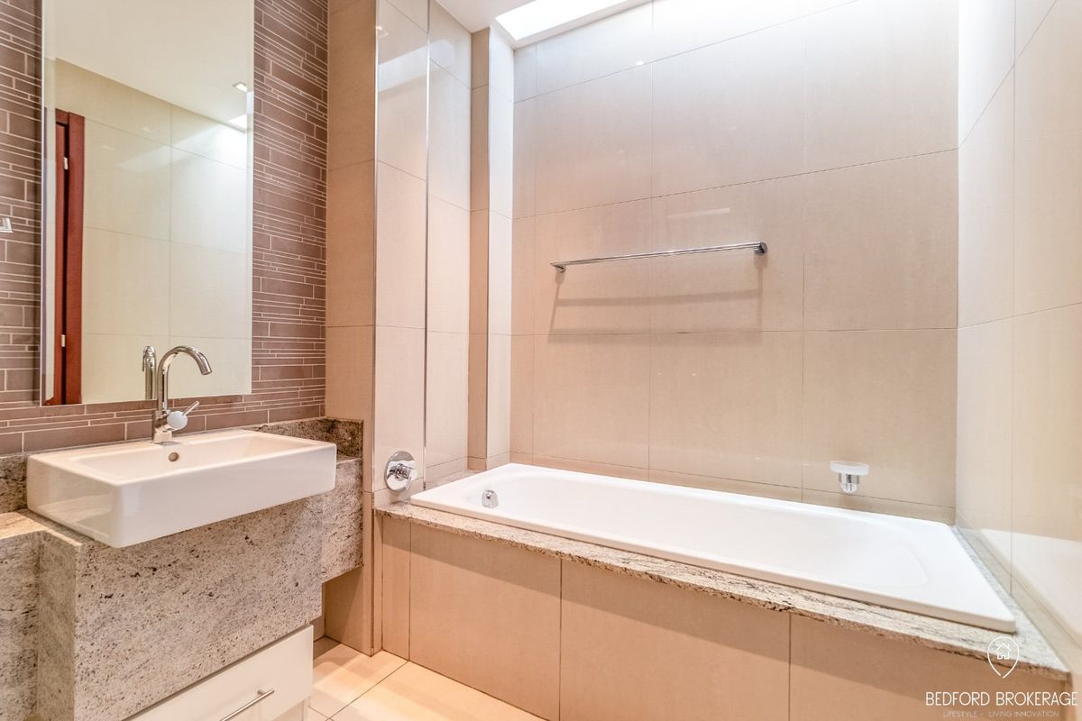 Modern bathroom featuring a built-in bathtub, granite vanity countertop, wall-mounted basin, and a skylight providing natural light.