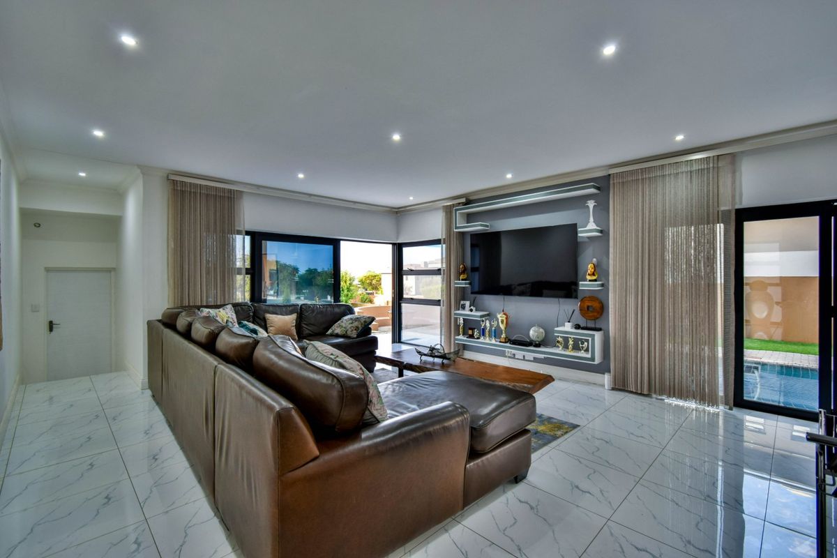 Modern living room featuring polished marble-look floor tiles, recessed downlighting, and a custom built-in media wall unit with direct access to the outdoor pool area.