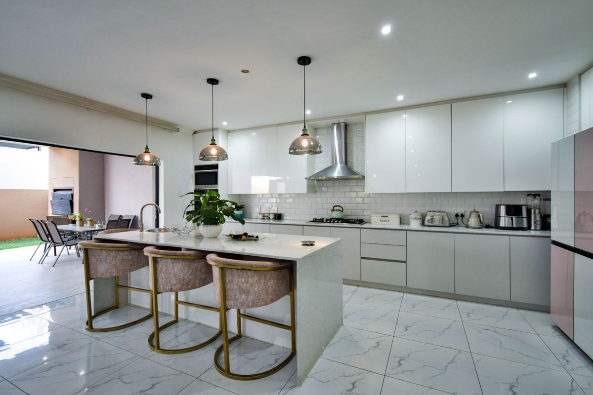 Modern kitchen featuring a large island with quartz countertops, high-gloss cabinetry, subway tile backsplash, and integrated appliances, flowing seamlessly to an outdoor patio area.