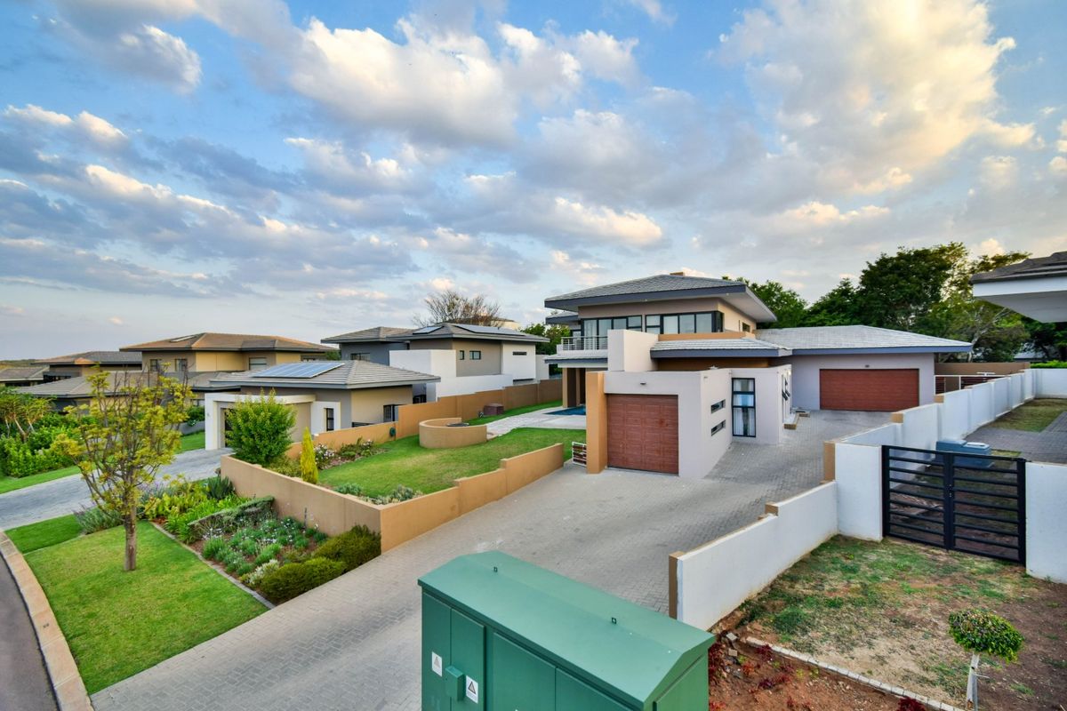 An elevated aerial view of a modern residential property featuring a paved driveway, double garage, and well-maintained landscaped garden within a secure estate.