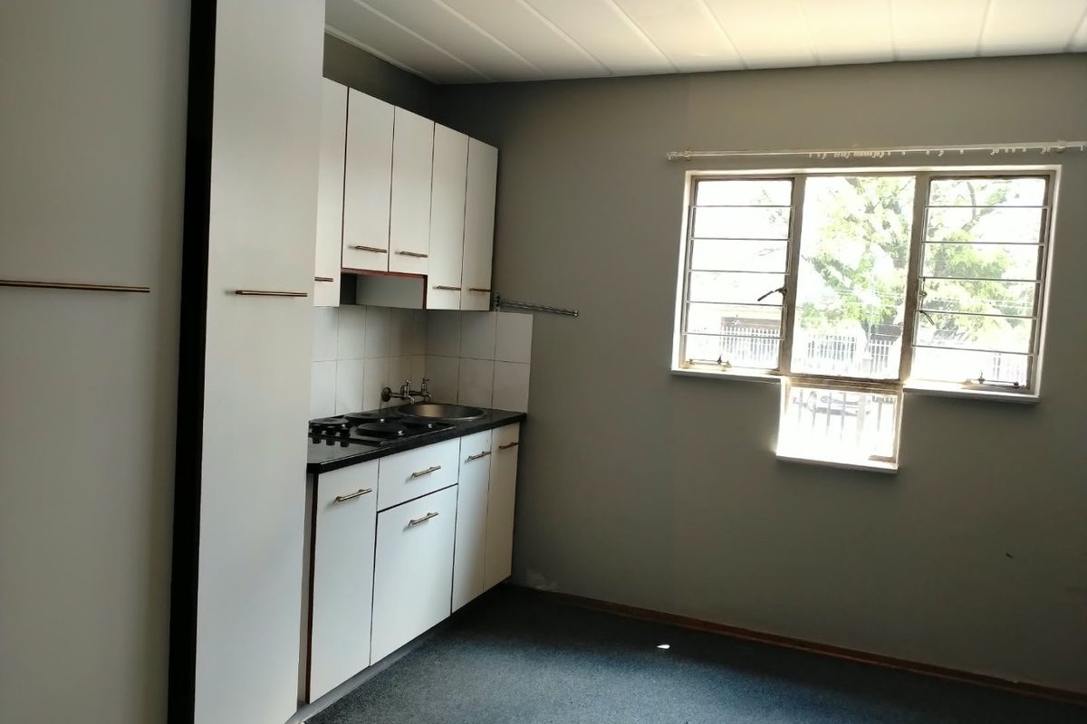 A compact, empty kitchen featuring built-in white cabinetry, a sink, and a hob, with a window providing natural light.