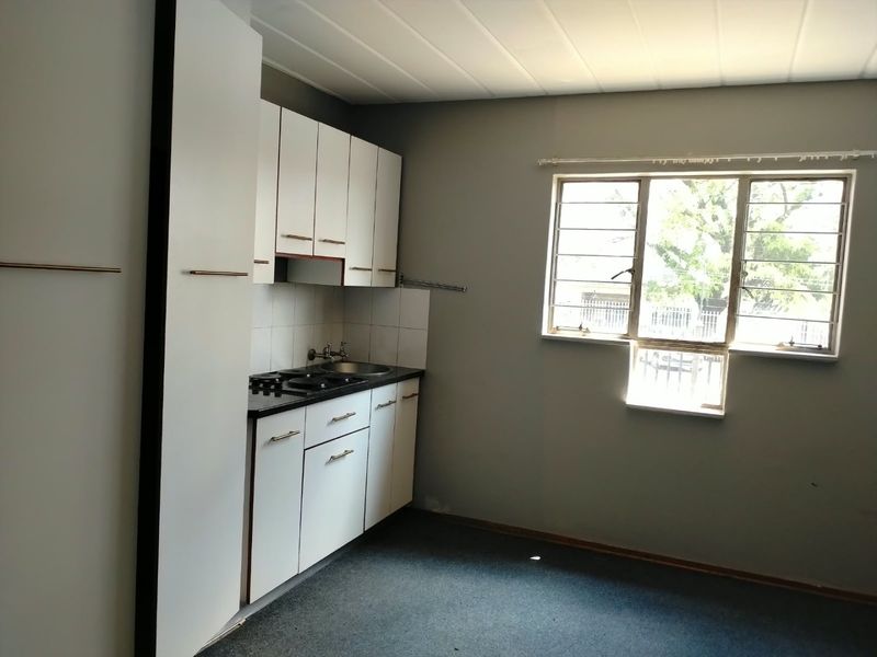 A compact, empty kitchen featuring built-in white cabinetry, a sink, and a hob, with a window providing natural light.