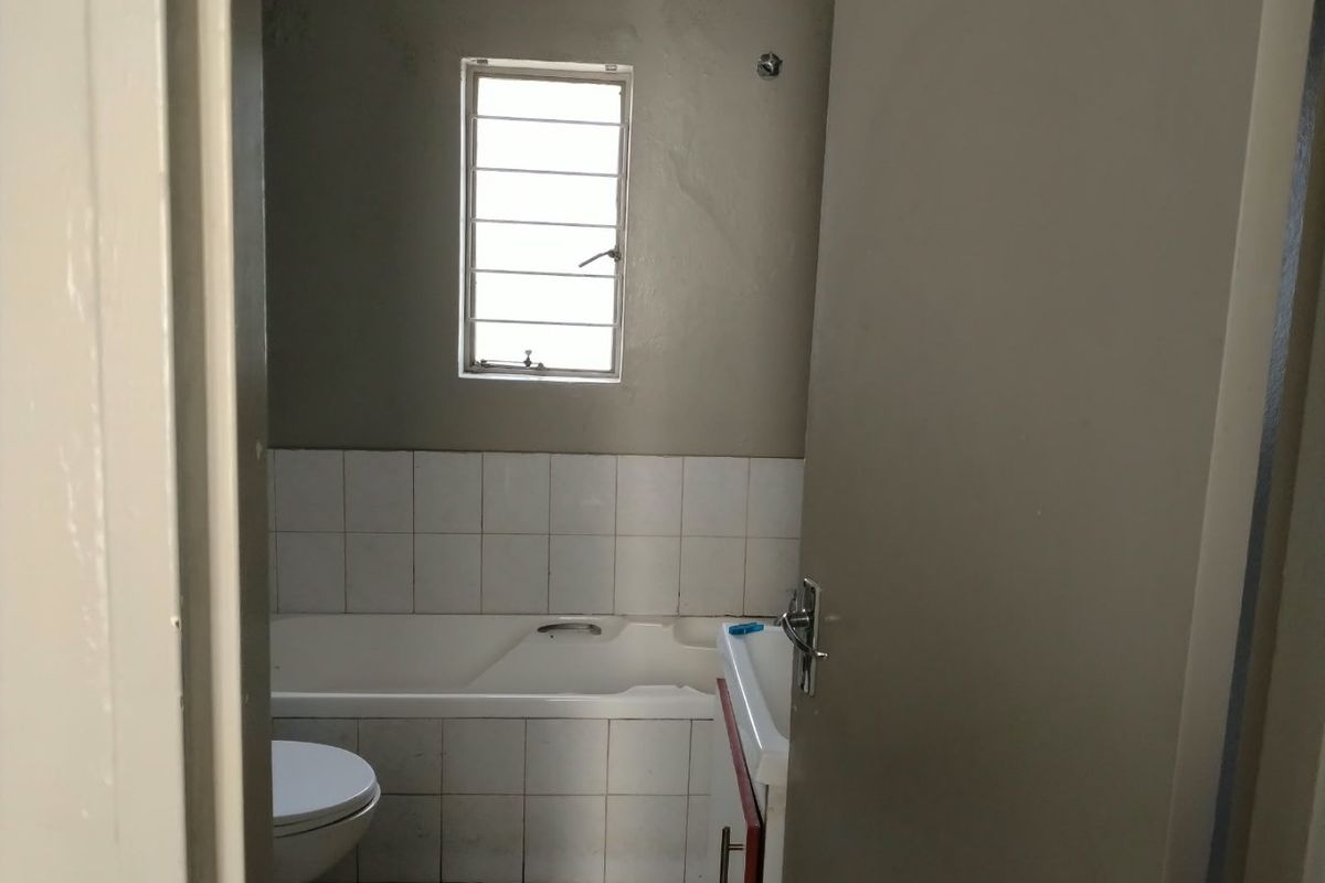 A functional bathroom featuring a bathtub, toilet, and vanity basin with tiled splashbacks and a louver window for ventilation.