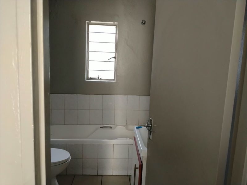 A functional bathroom featuring a bathtub, toilet, and vanity basin with tiled splashbacks and a louver window for ventilation.