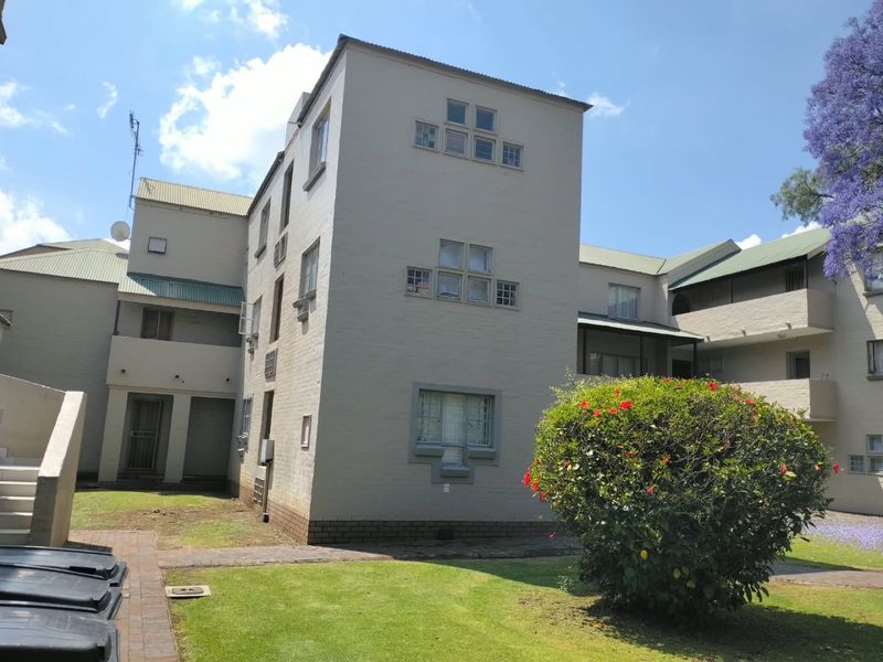 Exterior view of the apartment complex featuring a painted brick facade, metal roofing, and well-maintained communal garden areas.