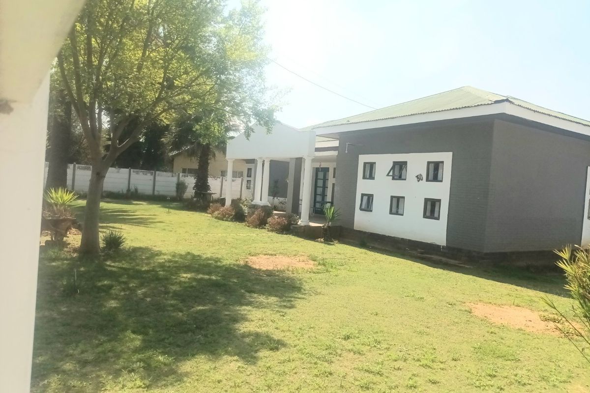Rear view of the property featuring a spacious garden, a covered patio area with columns, and a well-maintained exterior facade.