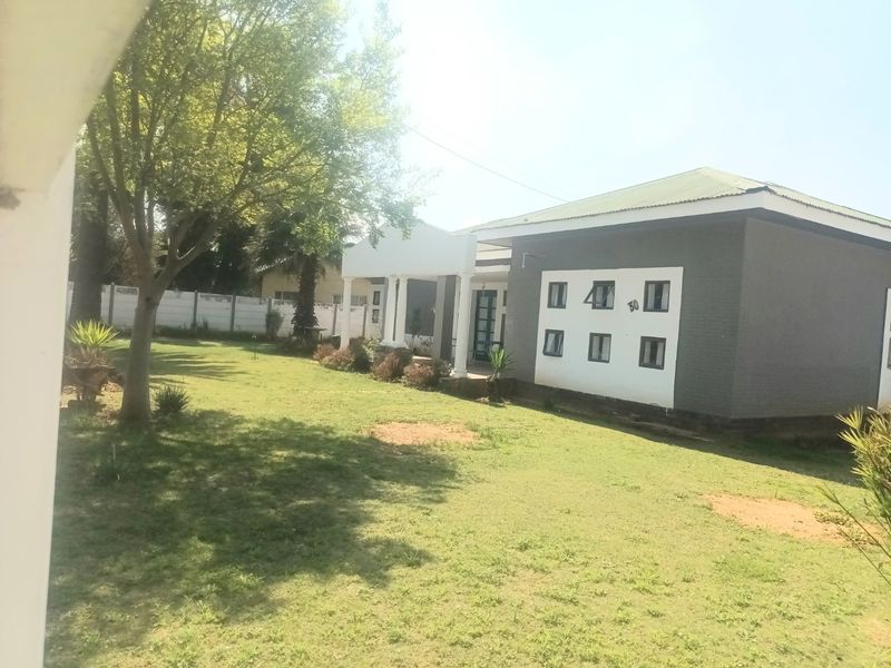 Rear view of the property featuring a spacious garden, a covered patio area with columns, and a well-maintained exterior facade.