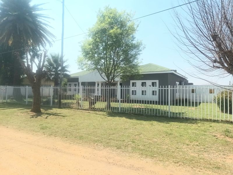 Front view of a single-story house featuring a pitched metal roof, covered entrance porch with columns, and secure metal perimeter fencing.