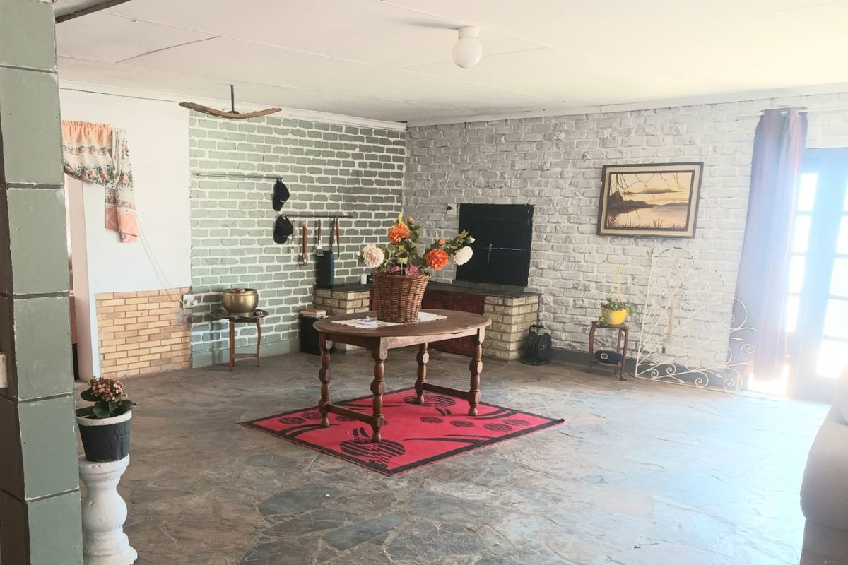 Spacious living area featuring rustic exposed brick walls, stone flooring, and a built-in fireplace, offering a blank canvas for renovation.